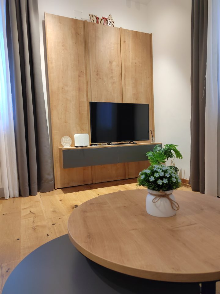TV zid i okrugli stolić sa cvijećem